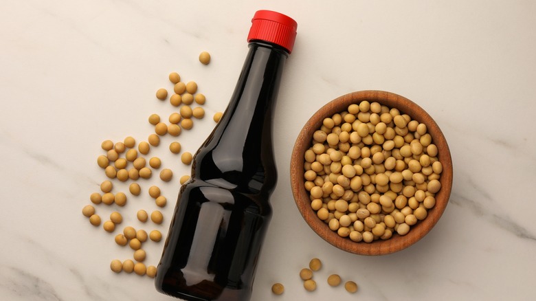 A bottle of soy sauce next to soybeans