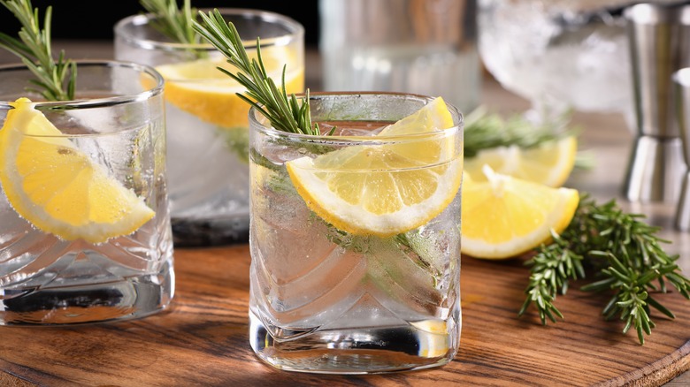 Three glasses of gin and tonix garnished with lemon slices and rosemary sprigs