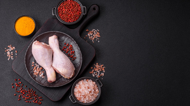 Two chicken drumsticks sit on a plate surrounded by salt and spices in little bowls