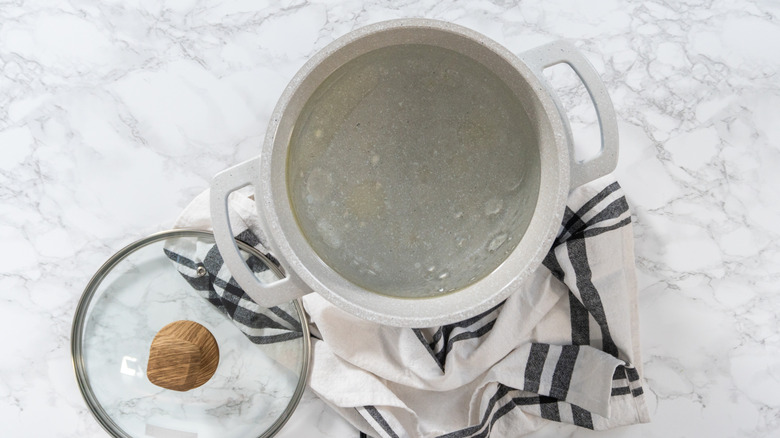 A pot of boiled water sits on a towel with the lid nearby