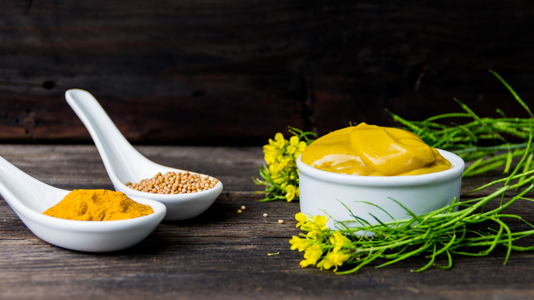 Jar of mustard with spoons of turmeric and mustard seeds