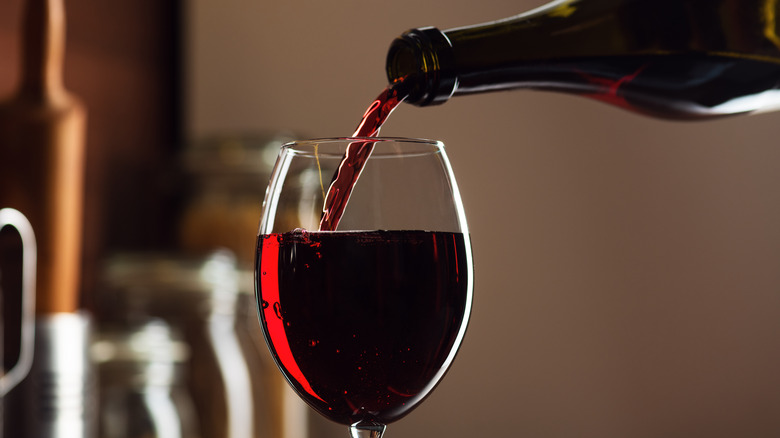 A bottle pouring red wine into a glass.