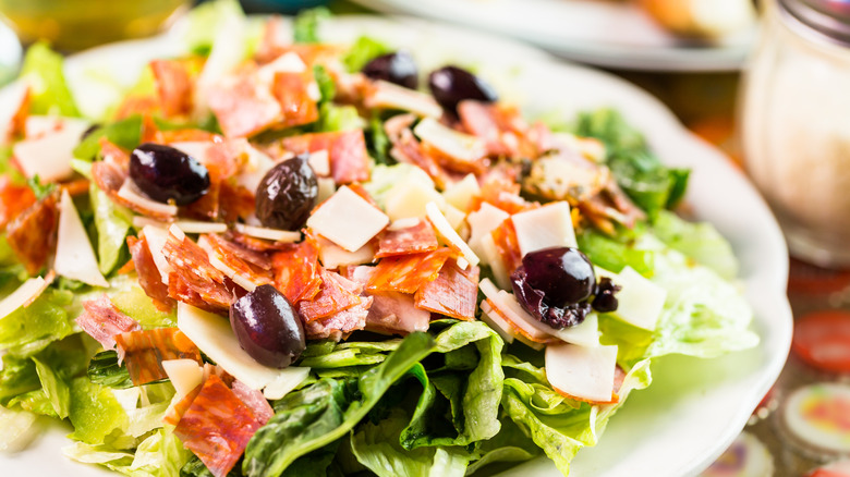 Salad topped with cured meats, cheese, and olives