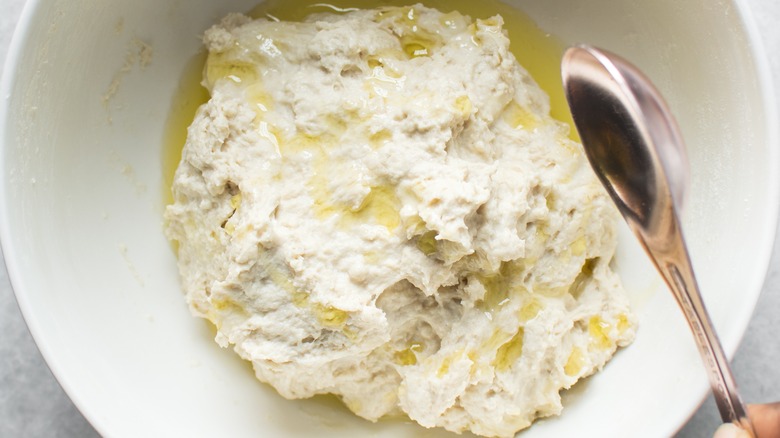 A spoonful of olive oil is added to a bowl of overproofed sourdough