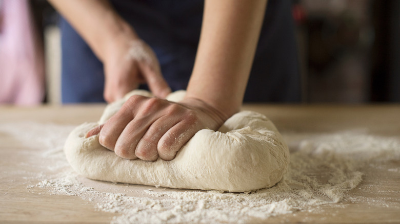 A baker kneads a batch of bread dough with their hands covered in flour