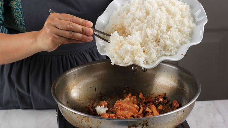 Chef adding white rice into pan of sauteed kimchi