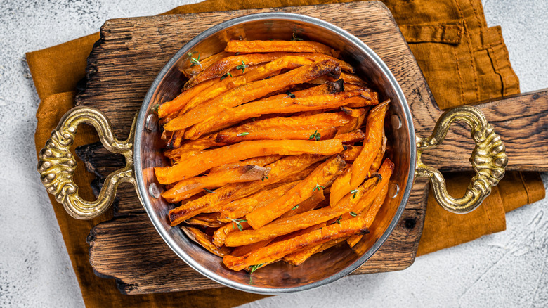 Roasted sweet potato french fries in a skillet with herbs. White background. Top view.