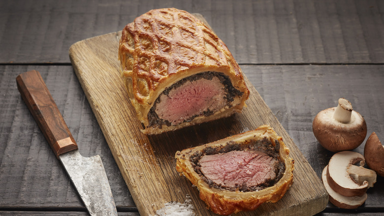 sliced beef Wellington on a wooden board, with a lattice pattern on the pastry crust