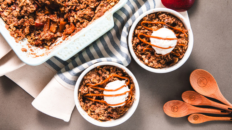 Two bowls of apple pie are topped with crumble and a scoop of ice cream.