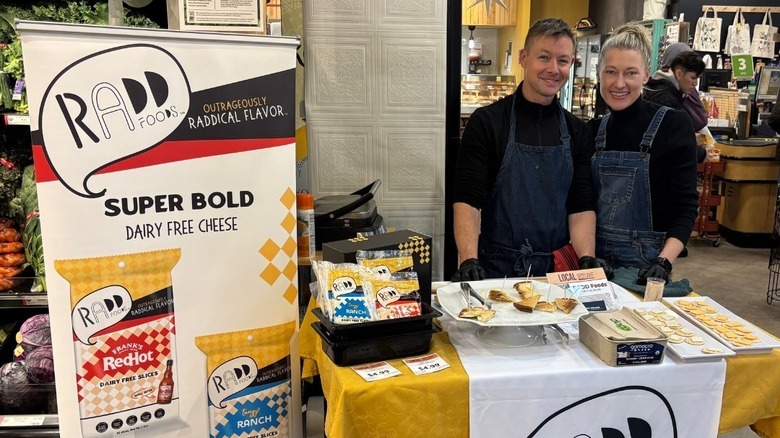 The two founders, Cole and Emily Williams, of RADD foods at a food stand in a market, giving away samples