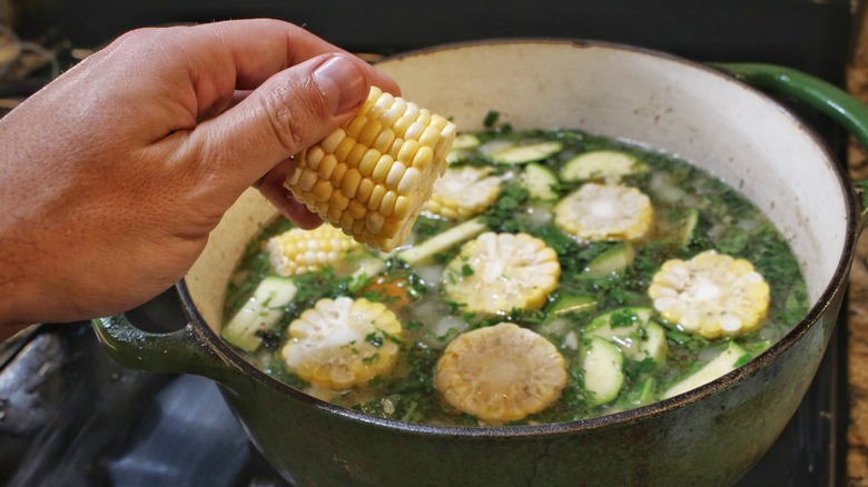 adding corn cob to soup pot