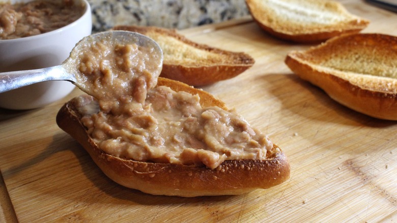 spreading refried beans on toasted rolls