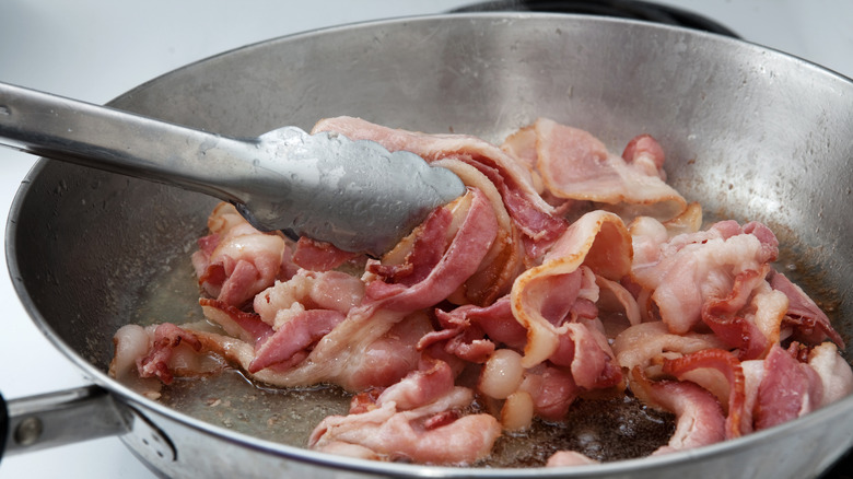 stirring bacon in pan with tongs