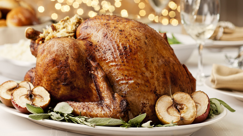 A roasted turkey sits on a bed of baked apples and fresh sage