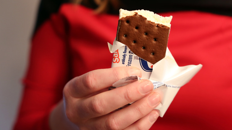 Person holding a half-eaten ice cream sandwich purchased from the grocery store