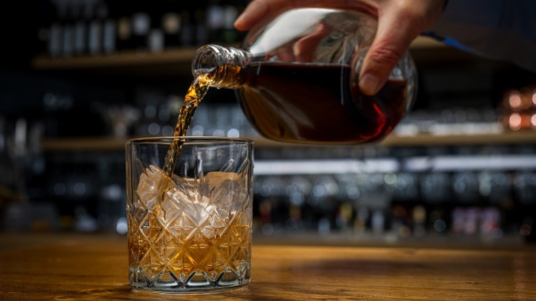 Person pouring a dark liquor into a glass 