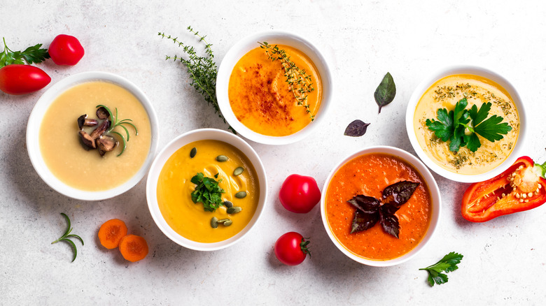 Different bowls of pureed soups in white bowls, including tomato, squash, and mushroom