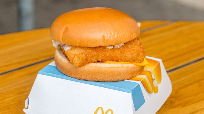 McDonald's Filet-o-Fish sandwich on top of its square blue and white cardboard box on a wooden table