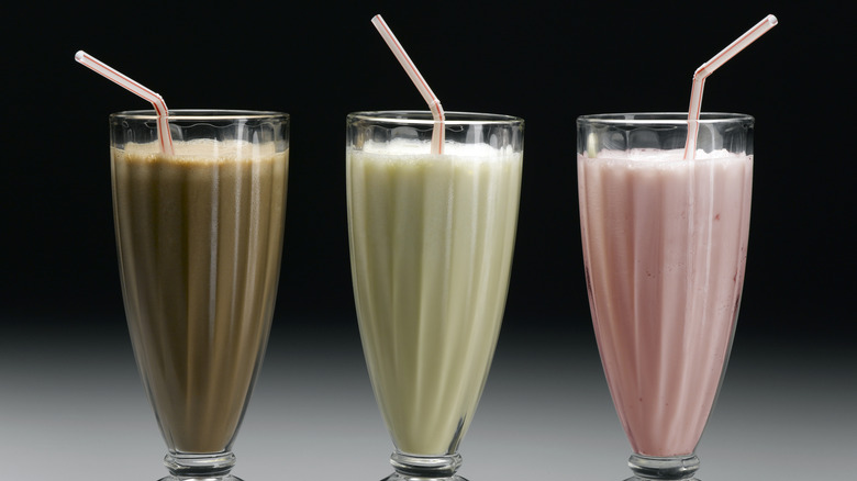 Chocolate, vanilla, and strawberry milkshakes in glass cups with a bendy straw