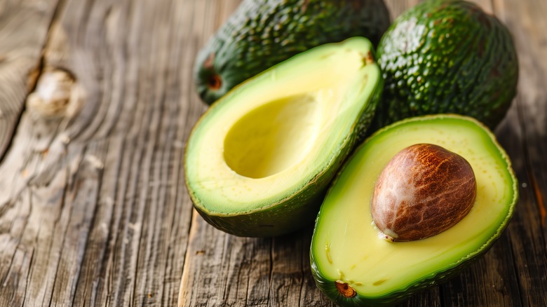 Ripe whole and sliced avocadoes on wooden boards