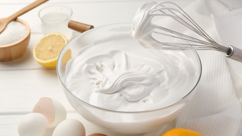 Whipped cream fills in a glass bowl with a wire whisk leaning on it.