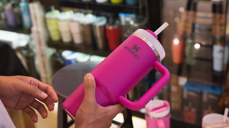 A person holds a bright pink Stanley mug with a lid in a store aisle