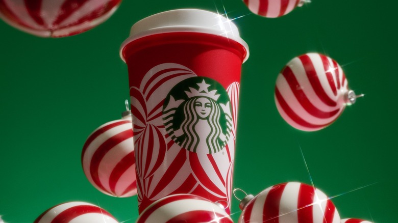 The new Starbucks holiday themed red reusable cup sits with red and white striped ornaments on a green background