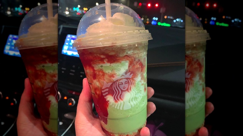 Hand holds a Grande Starbucks Matcha Crème Frappuccino with strawberry puree