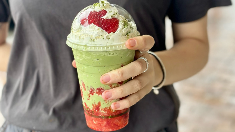 A matcha frappuccino is lined with strawberry puree and topped with whipped cream, matcha powder, and fresh strawberries