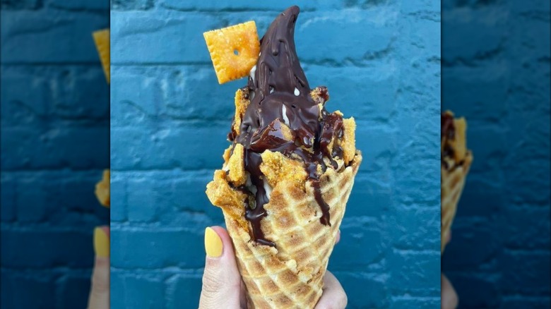 A hand holds an ice cream waffle cone with chocolate shell and Cheez-its