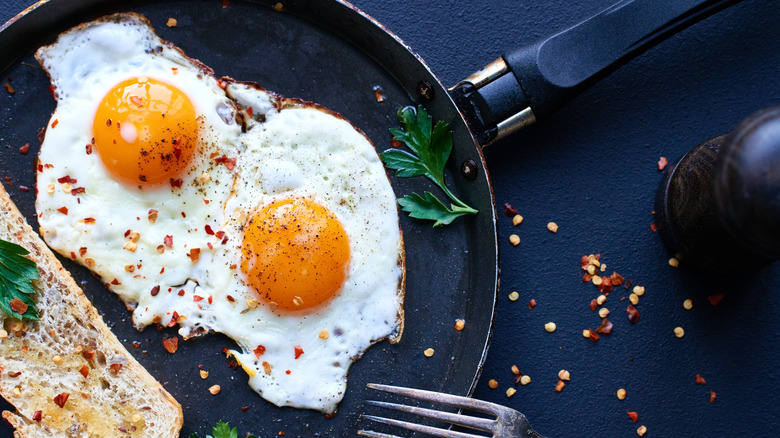 Two fried eggs in black pan with bread and red pepper flakes