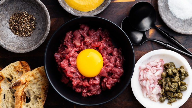 Steak tartare with egg yolk in bowl plus add-ins