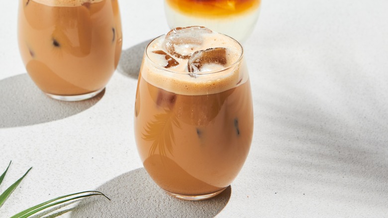 Iced latte in glass with ice cubes on white surface