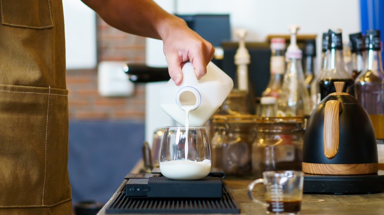 Barista pouring milk from a jug into a small glass