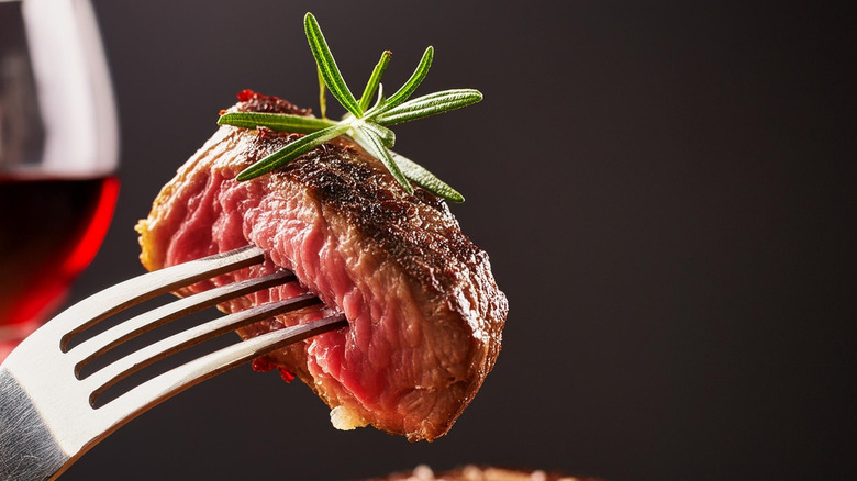 A piece of grilled steak on a fork with a sprig of rosemary.