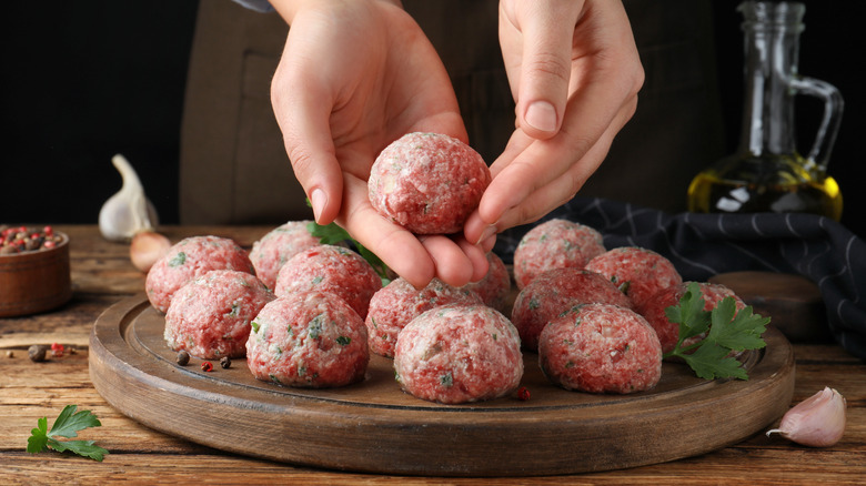 Hands rolling meatballs over round wooden cutting board