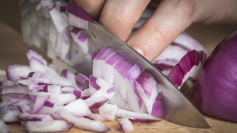 Close up of sharp knife chopping red onions
