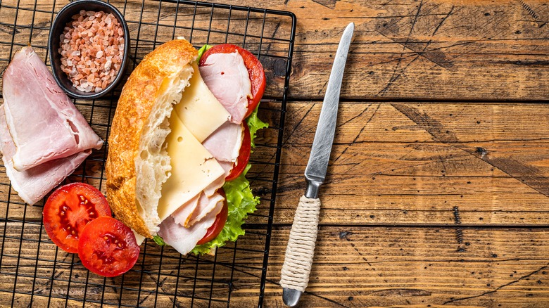 Hoagie with ingredients and knife on wood table