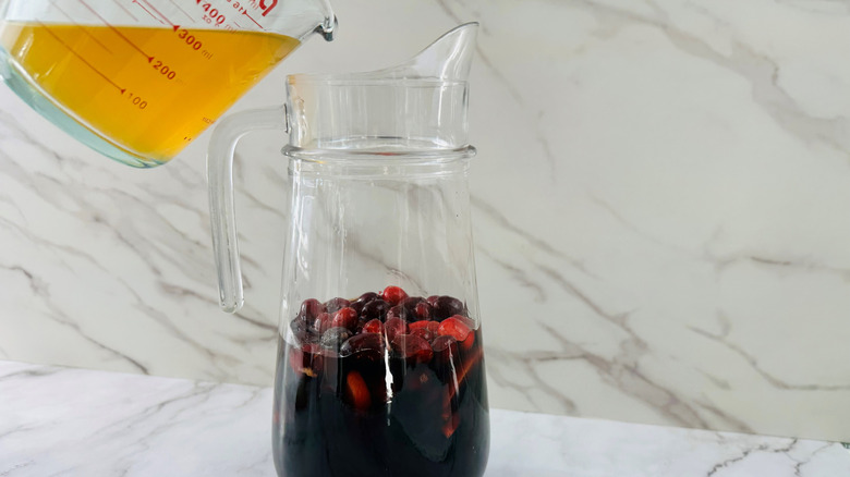 Apple cider pouring into a jug with rum, fruit, and wine