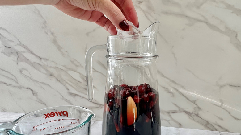 Hand adding ice cubes to a glass jug of sangria