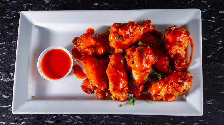 A plate of hot wings with a ramekin of hot sauce rests on a black granite table