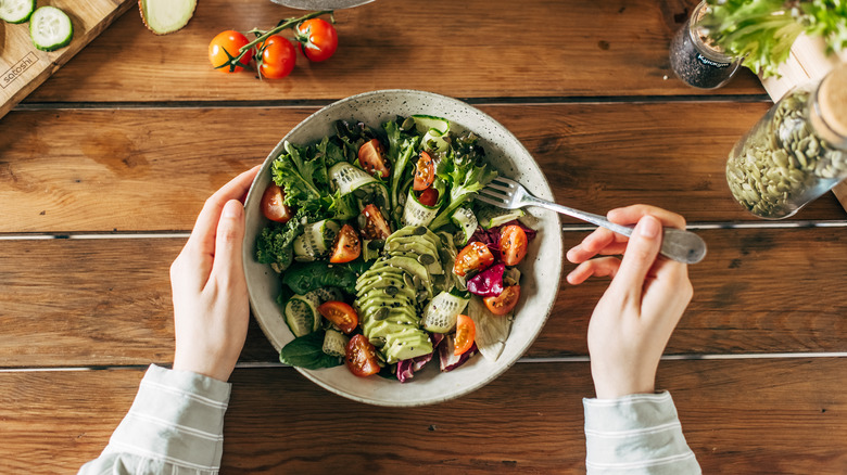 Bowl of salad surrounded by various salad ingredients