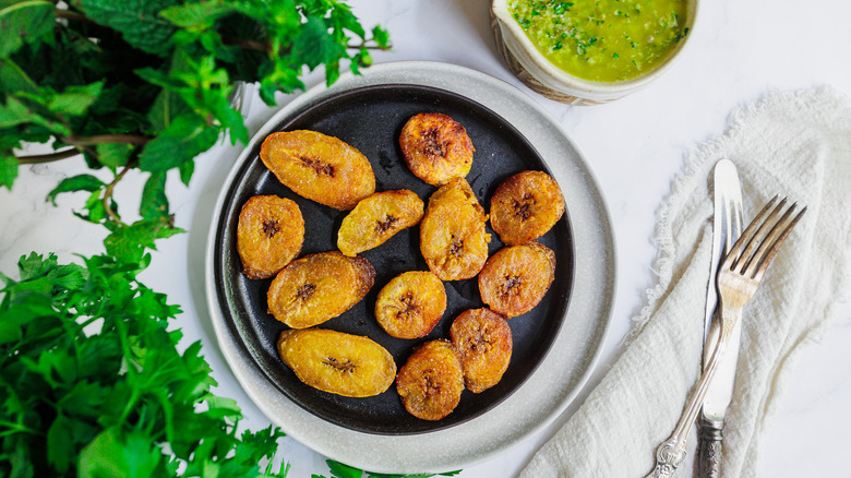 Fried plantains on plate with herbs and sauce on the side