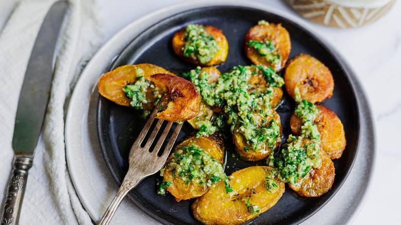 fried plantains with green sauce on black plate with one speared on fork