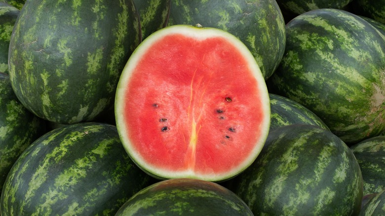 halved watermelon on top of whole watermelon pile