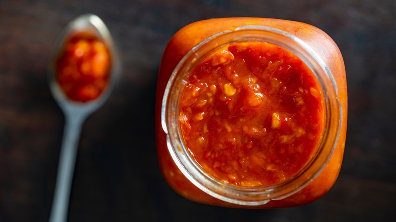 An open jar of rustic tomato sauce with a spoon beside it