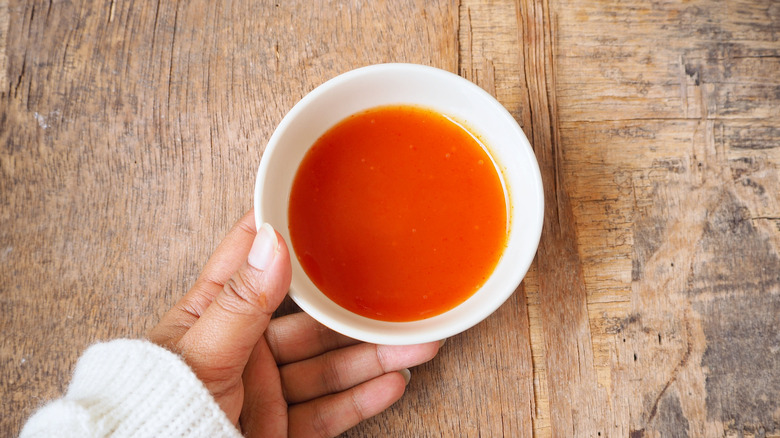 a hand holding a bowl of sriracha