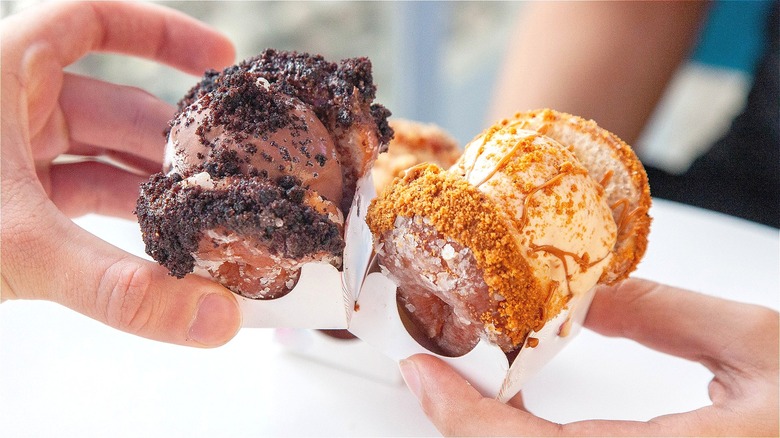 Two hands holding two mini, crumb-covered donut ice cream sandwiches