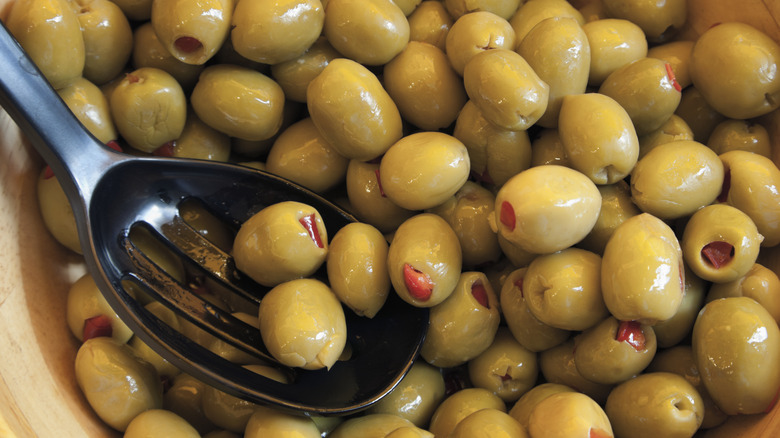 Metal spoon picking up a batch of green olives from a bowl