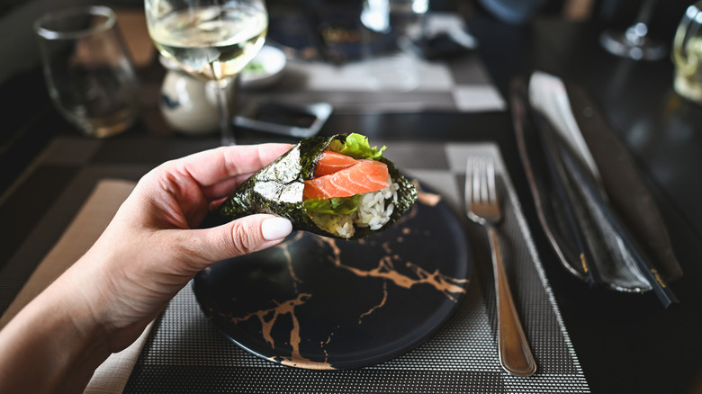 Diner holding a temaki roll in a fine restaurant